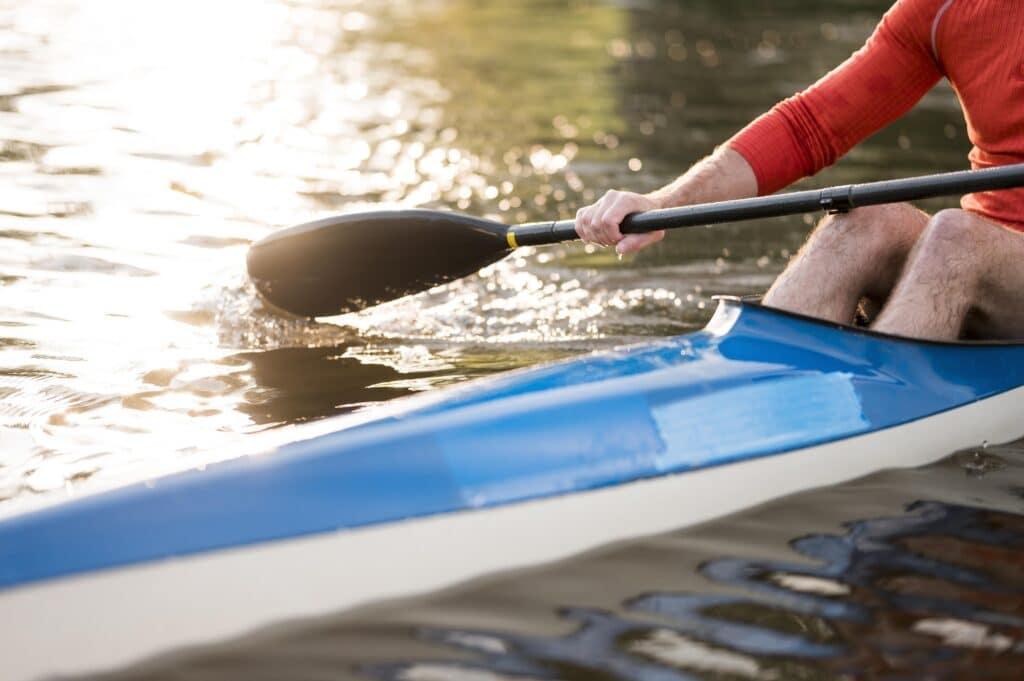 Kayak bleu et pagaie au soleil couchant : Sport nautique Kayakiste pagayant dans un kayak bleu sur une eau étincelante au coucher du soleil, mouvement de pagaie.
